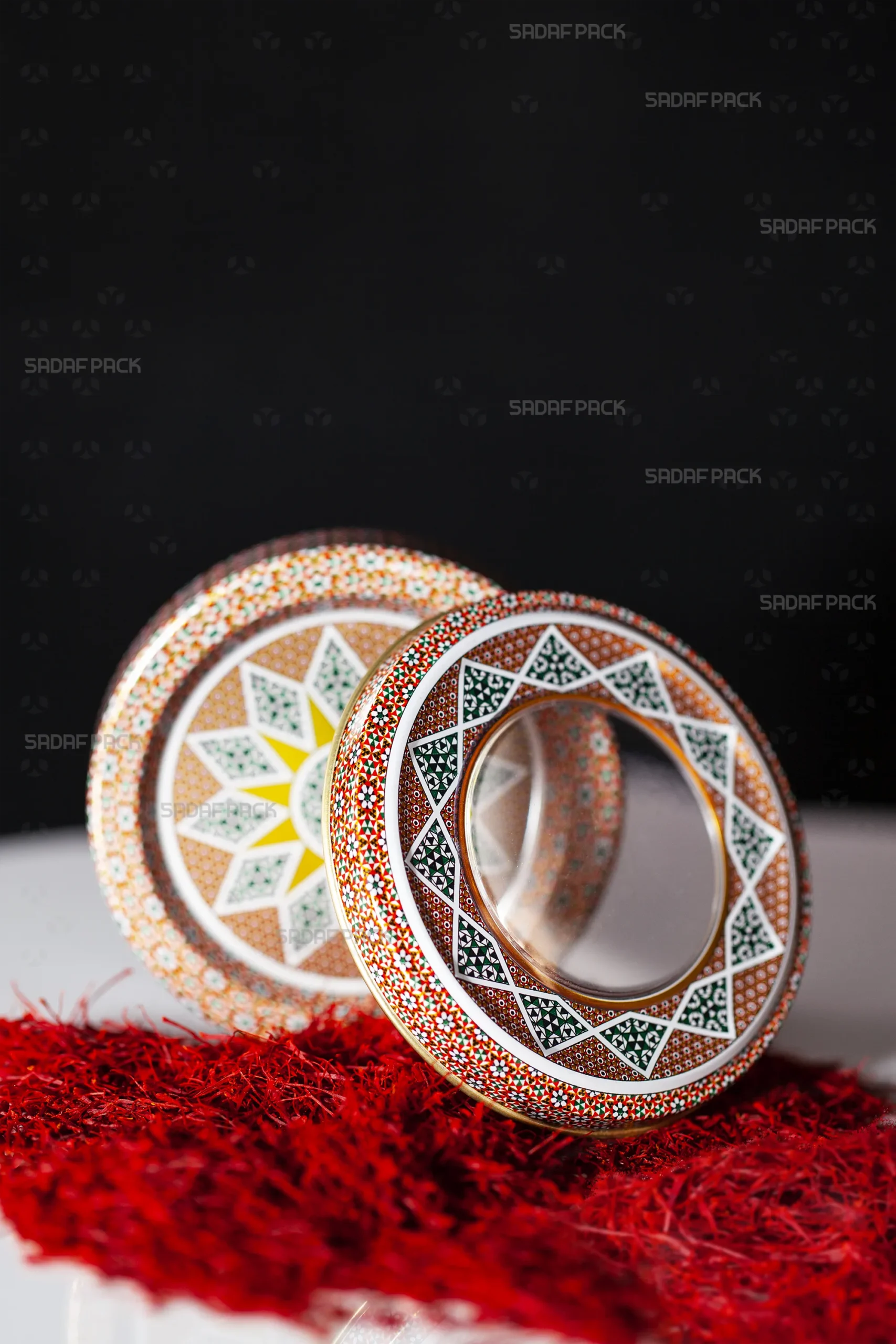 عرض وصفي لعلبة صدف باك المعدنية سعة 5 جرام بتصميم "خاتم أحمر"، يظهر الغطاء المزخرف بنافذة شفافة على شكل حلقة والقاعدة المطابقة له، وهما معروضان بشكل منفصل على طبقة من خيوط الزعفران الأحمر الزاهي.