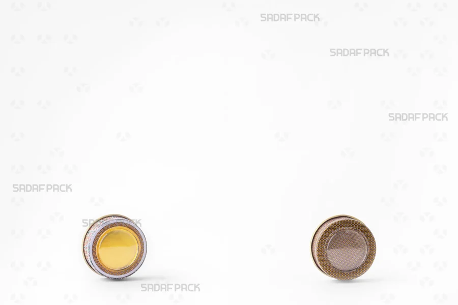 A side-by-side comparison of two different 1-gram metal tin designs, showcasing the distinct patterns and colors used for Sadaf Pack's premium saffron packaging.