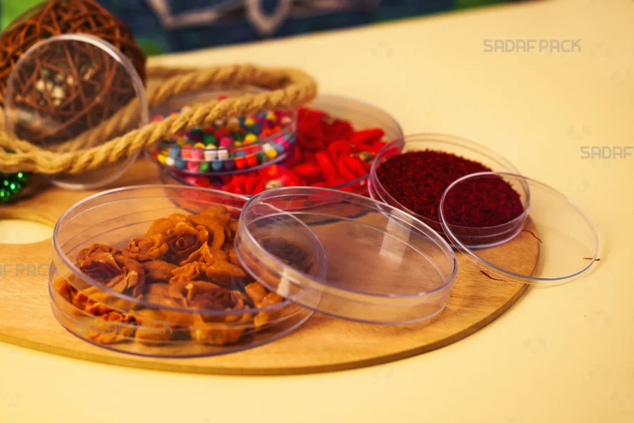 A collection of Sadaf Pack's deep, circular crystal containers in various sizes, elegantly displaying vibrant saffron threads, delicate rose-shaped sweets, and colorful candies on a wooden surface to showcase their use for luxury food packaging.