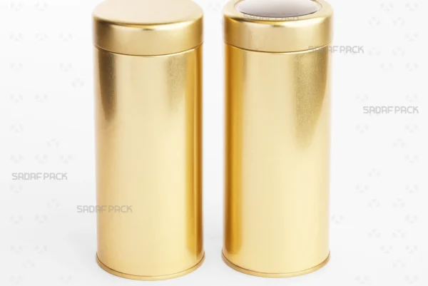 A comparative view of two tall Sadaf Pack 6.6x13.5 cm solid gold metal tins, displayed together to contrast the transparent window lid version against the solid lid version.
