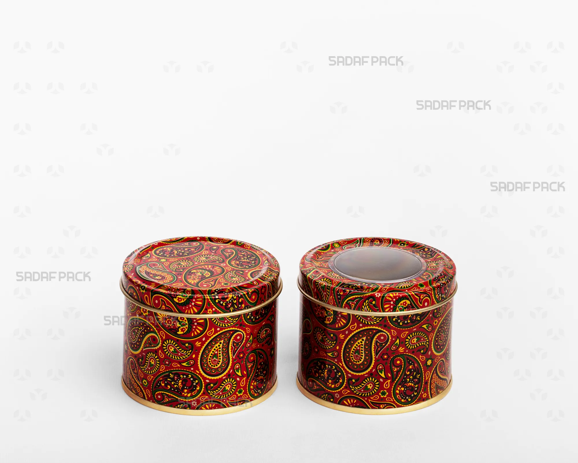 A side-by-side comparison in a three-quarter view of two Sadaf Pack 7cm by 5cm metal tins with the Red Termeh pattern, both closed, showing the version with a polycrystal window lid and the version with a solid lid.