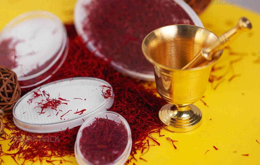 عرض حيوي لعبوات صدف باك البيضاوية من طراز إسبانيا، تُظهر خيوط الزعفران الأحمر الفاخرة بجانب هاون ومدقة ذهبية تقليدية على خلفية صفراء زاهية، مما يبرز ملاءمتها لتغليف التوابل الفاخرة.