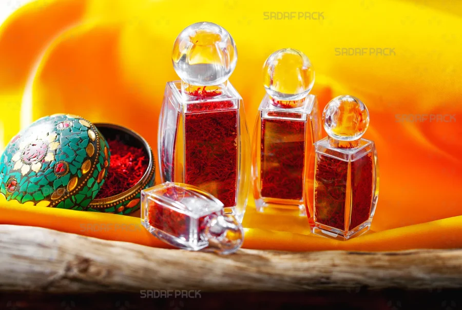 A collection of Sadaf Pack's sadaf crystal containers of various sizes, filled with vibrant red saffron threads, elegantly arranged on a wooden surface against a flowing golden-orange satin background.