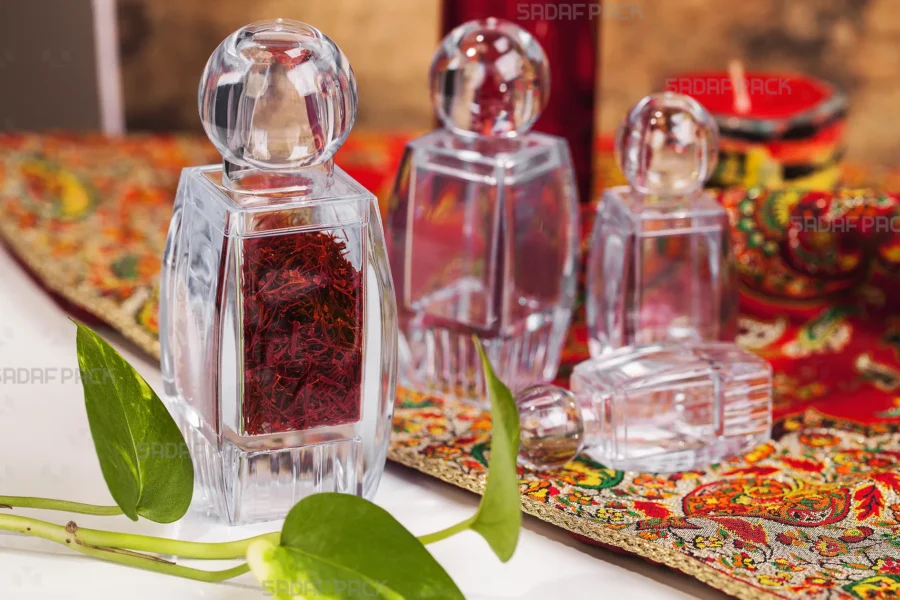 مجموعة من عبوات كريستال صدف الفاخرة من صدف باك، إحداها مملوءة بخيوط الزعفران الأحمر الفاخر، مرتبة بأناقة على نسيج تقليدي منقوش لإبراز ملاءمتها لتغليف التوابل الراقية.